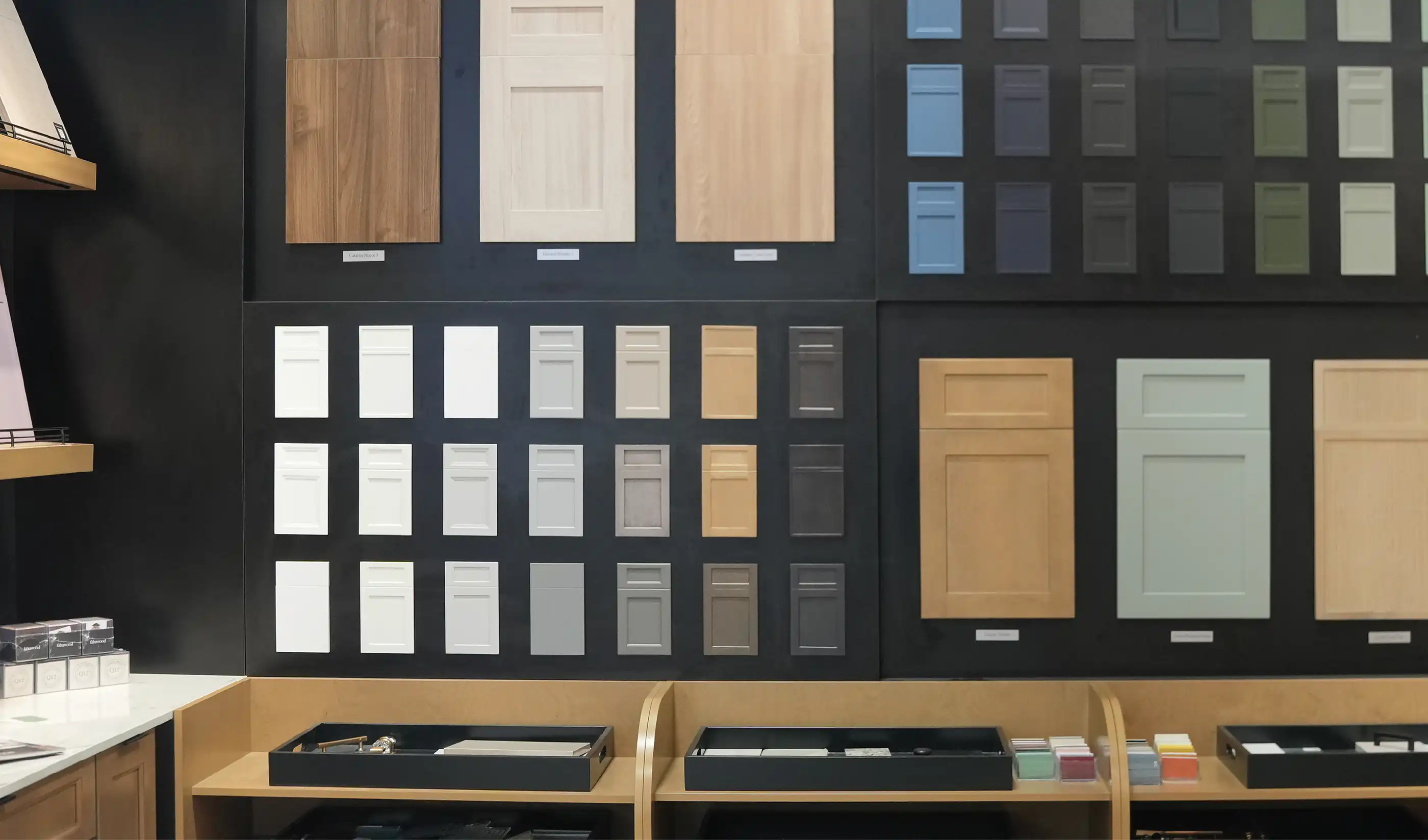 A dark display wall of cabinet door samples: wood, white, gray, blue and green doors in shaker and slab styles