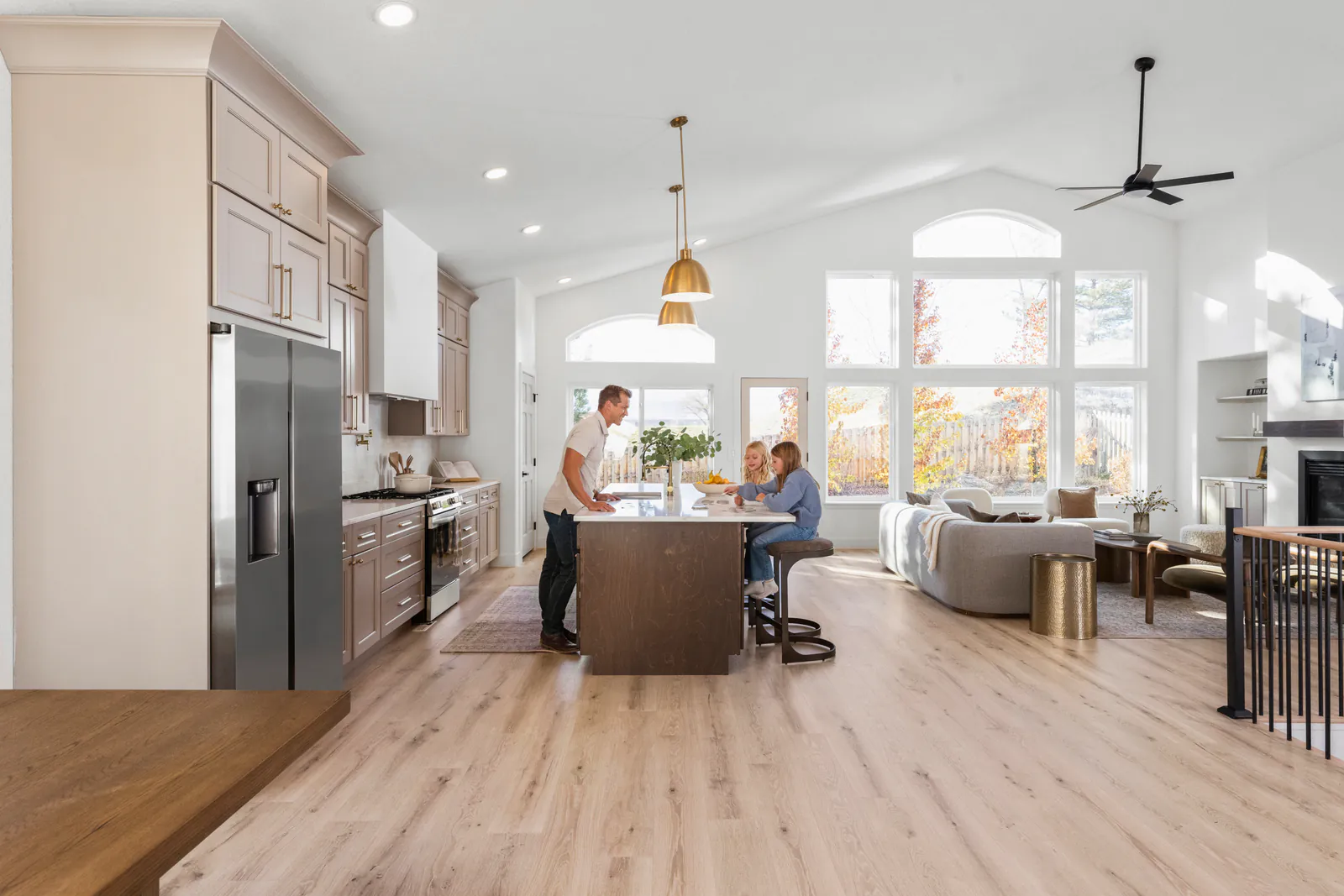 A dad and two kids at a dark stained wood island in a kitchen with taupe shaker cabinets up to the ceiling and brass pendant lights