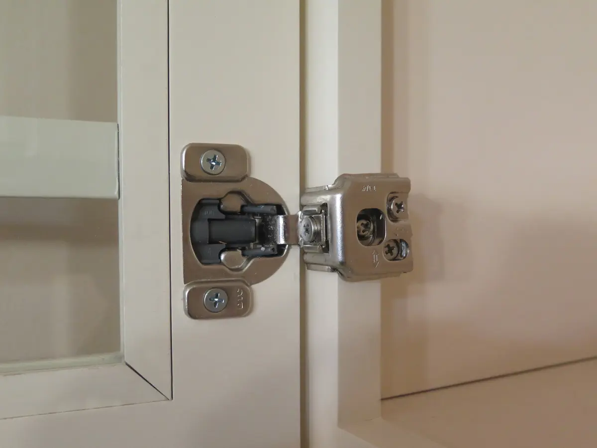 A soft-close hinge on an open ivory cabinet door, one of its screws ringed in gold
